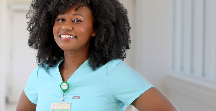 Smiling healthcare professional in light blue scrubs with a clip-on badge.