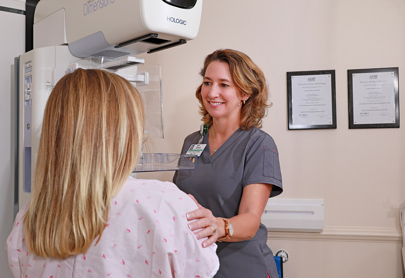 A smiling imaging tech helping a patient with a mammogram.