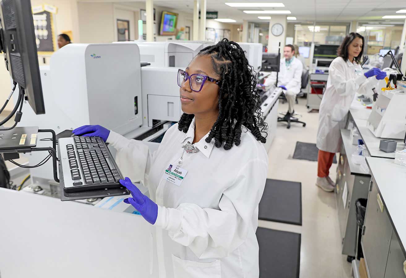Lab technicians testing lab samples and reviewing results on a computer. 